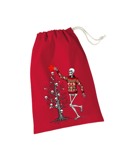 rotes Geschenksackerl aus Baumwolle mit Zugkordel mit weihnachtlichem Design: Skelett in rotem Weihnachtspulli schmückt kahlen Weihnachtsbaum mit Totenköpfen und Knochen, steckt gerade roten Stern oben drauf