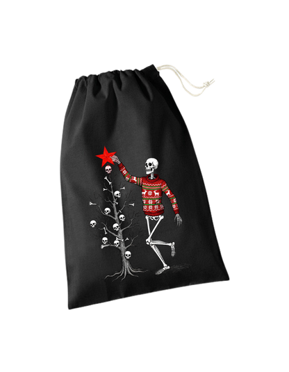 schwrzes Geschenksackerl aus Baumwolle mit Zugkordel mit weihnachtlichem Design: Skelett in rotem Weihnachtspulli schmückt kahlen Weihnachtsbaum mit Totenköpfen und Knochen, steckt gerade roten Stern oben drauf
