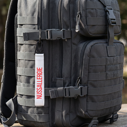 schwarzer taktischer Rucksack mit weißem Schlüsselanhänger und roter Schrift:Nussallergie" zum Veranschaulichen des Anhängers