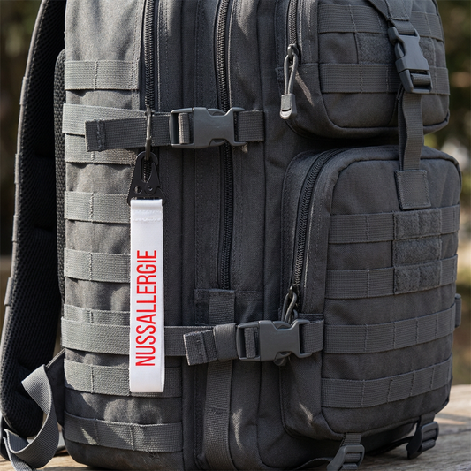 schwarzer taktischer Rucksack mit weißem Schlüsselanhänger und roter Schrift:Nussallergie" zum Veranschaulichen des Anhängers